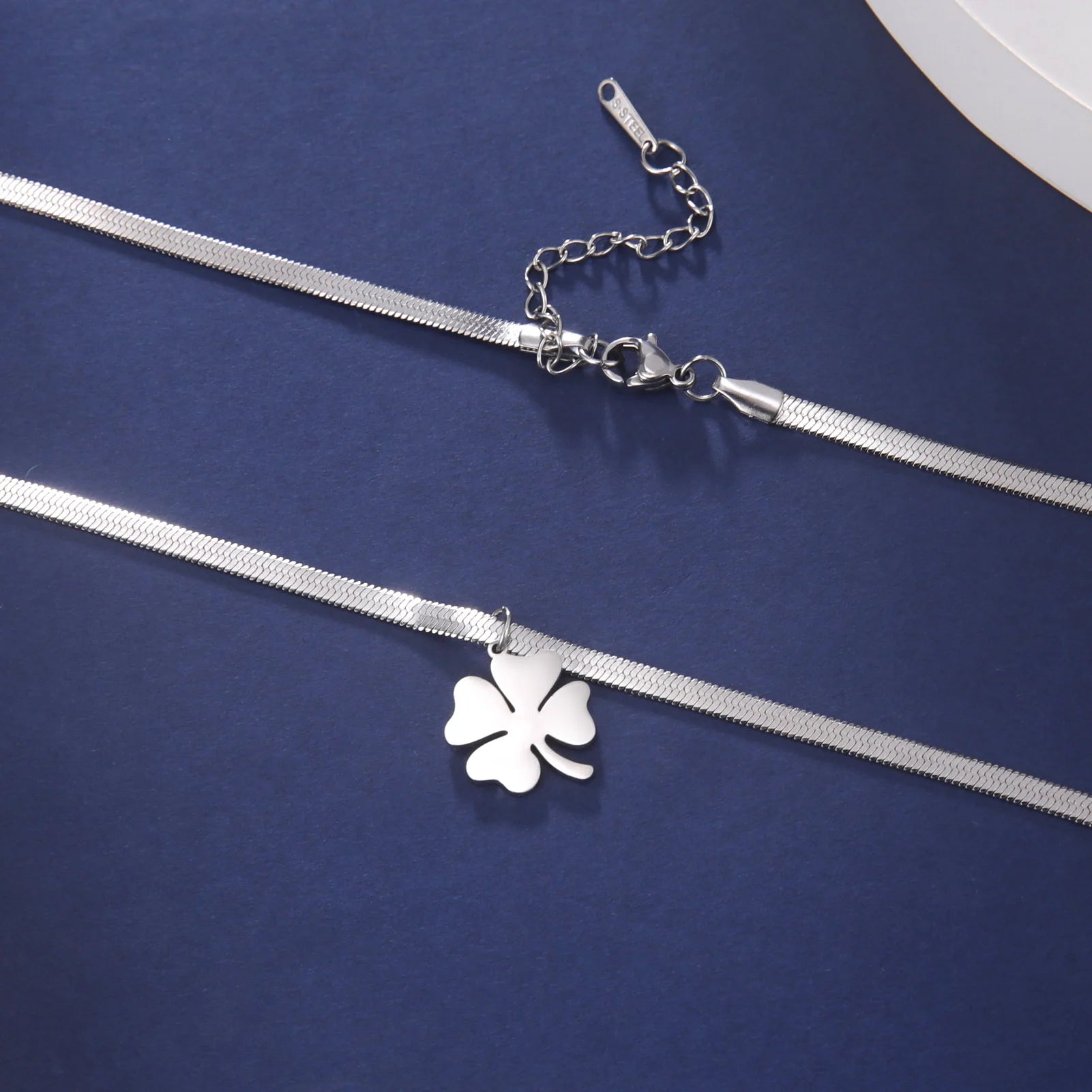 Silver clover necklace with extension chain and clasp laid flat on blue background