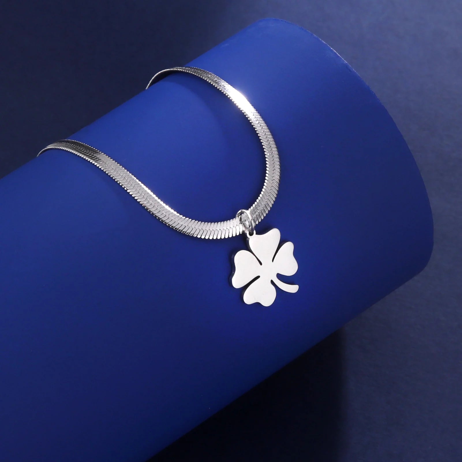 Silver clover pendant necklace laid on blue cylindrical display