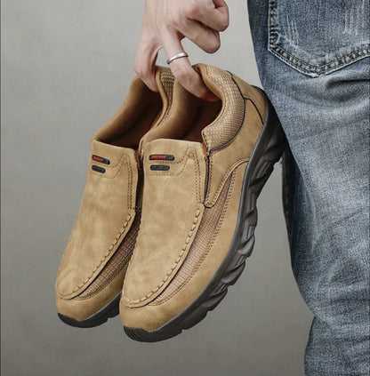 Tan leather loafers held in hand, showcasing soft upper and rugged sole