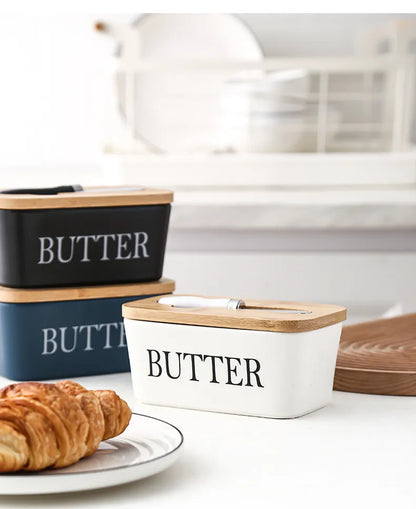 White ceramic butter dish filled with butter, shown with stacked black butter dishes and bamboo lids in modern kitchen