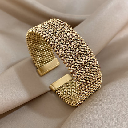 Wide gold mesh cuff bracelet on beige fabric, top view